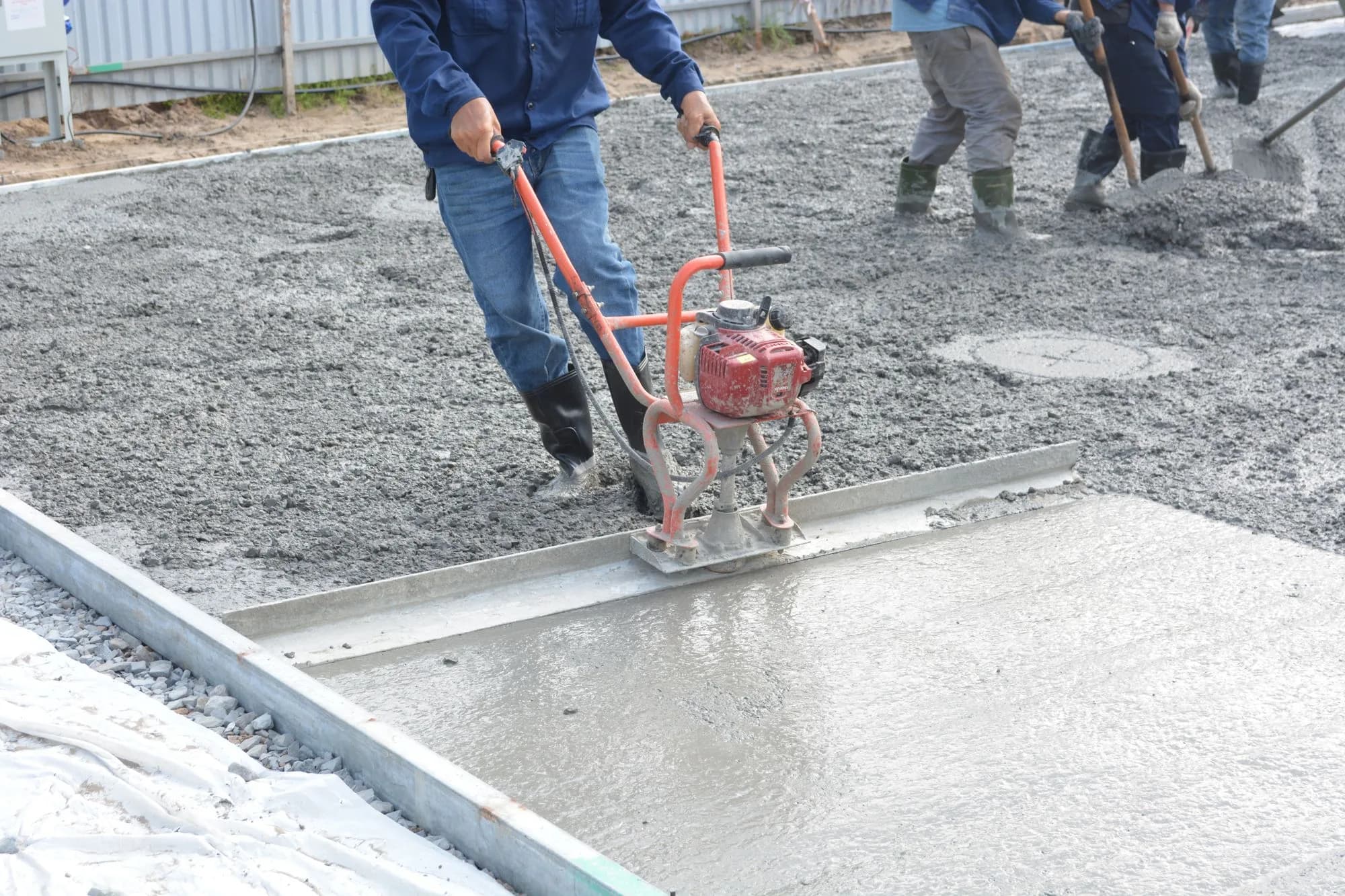Construction workers using power tools to level freshly poured concrete for a deck footing, showing correct deck footing size and depth