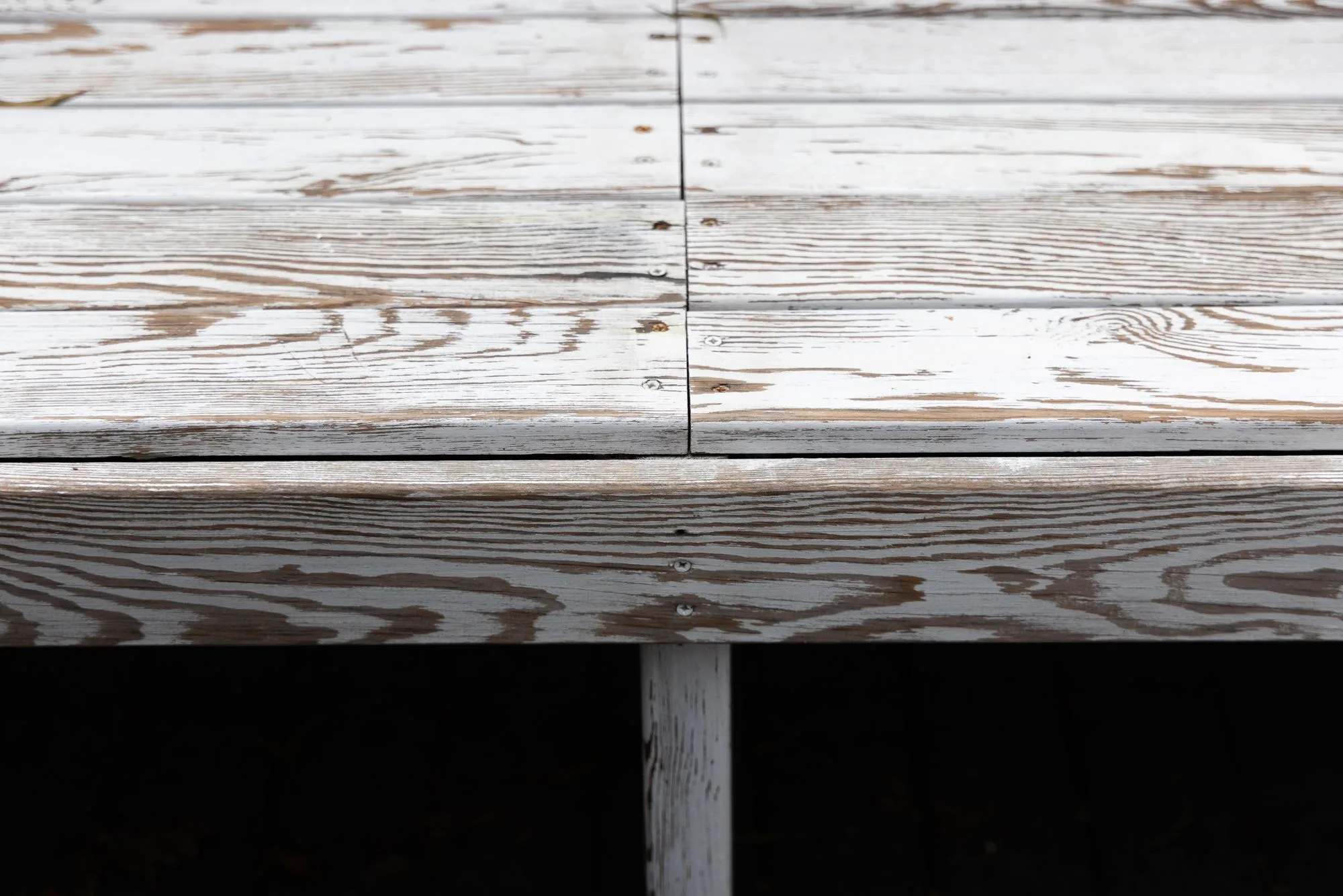 Close-up of aged wooden deck planks with visible screws, showing weathered texture near a ledger board attachment