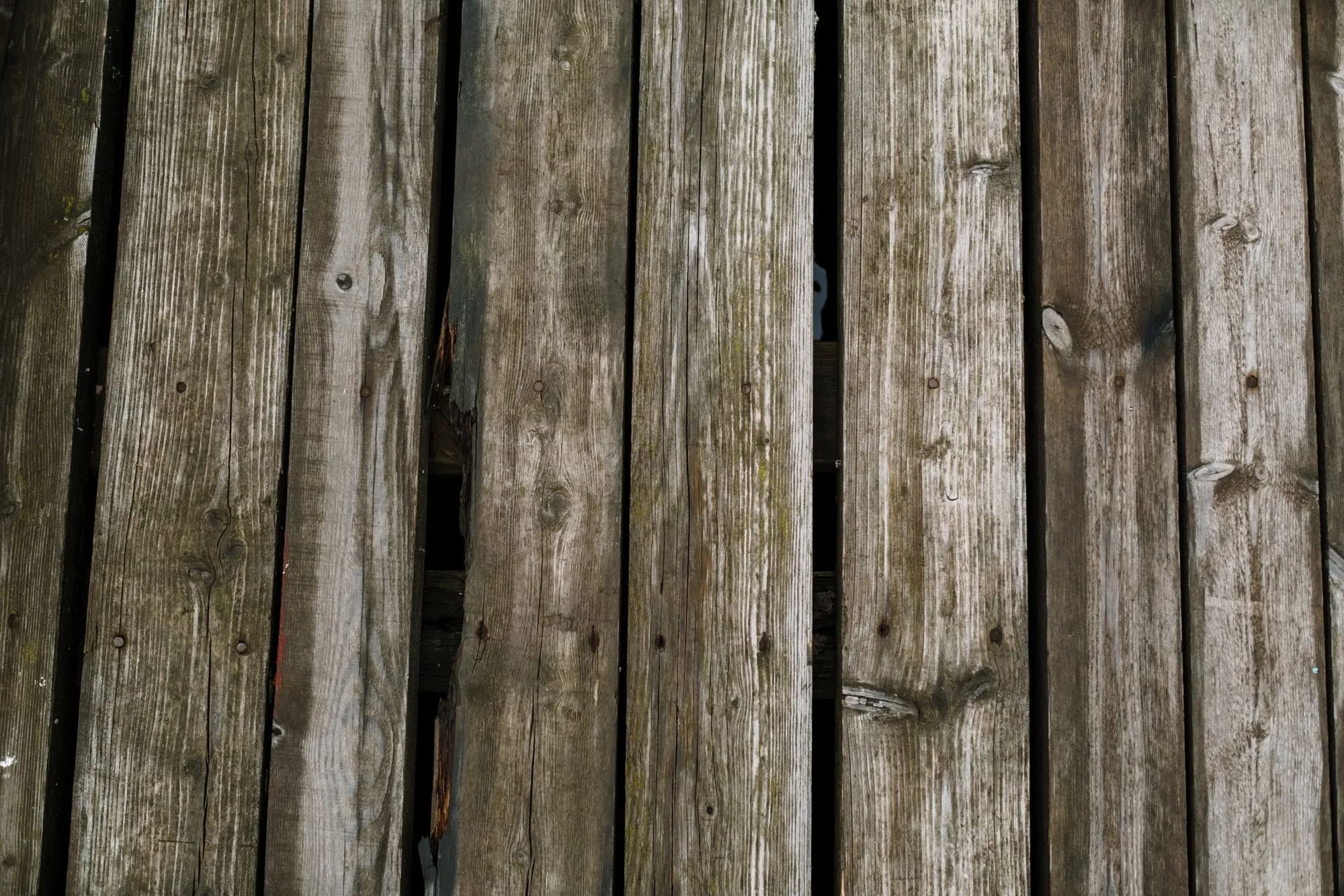 Close-up of aged, weathered wooden deck planks showing splitting grain and worn fasteners
