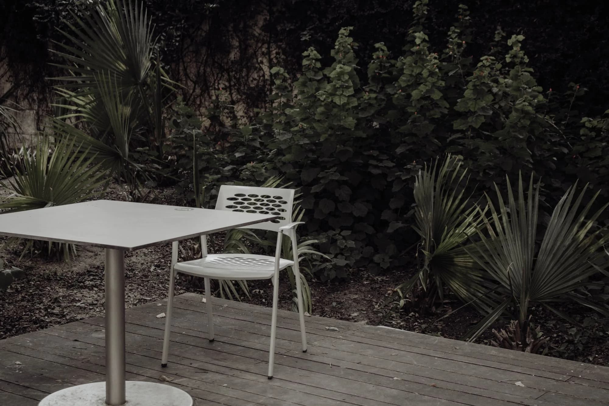 A tranquil outdoor deck setting with a modern chair and table surrounded by lush green plants