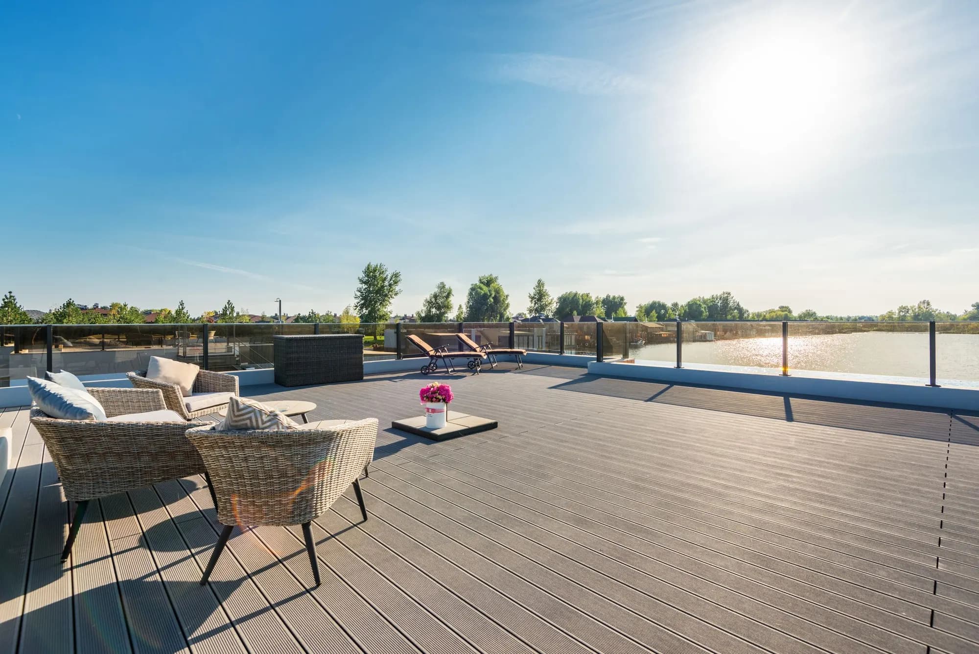 A spacious lakeside timber deck with lounge furniture in afternoon sun